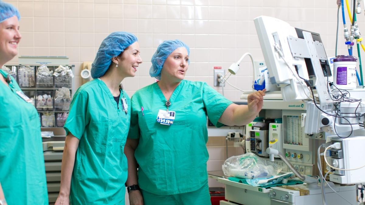 Three nurses observe a monitor in an operating room